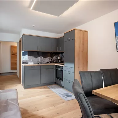 A modern kitchen with wooden furniture and a dining table. The room is designed to be bright and welcoming.