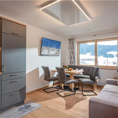 A modern, bright holiday apartment with an open kitchen and dining area. Large windows provide a view of the snow-covered landscape.