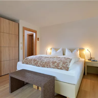 A modern bedroom with a comfortable double bed and wooden furniture. The warm colors create an inviting atmosphere.