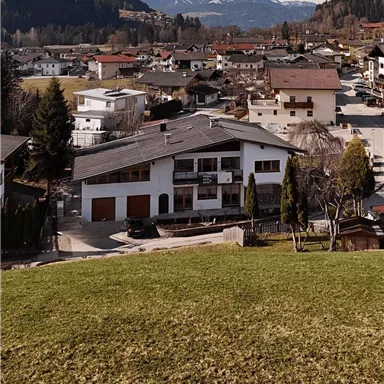 Ein malerisches Dorf mit einer ruhigen Wohngegend und Bergen im Hintergrund. Die Häuser sind umgeben von Wiesen und Bäumen.