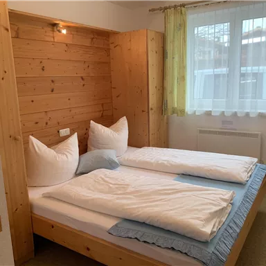 A cozy bedroom with a double bed and wood paneling. Natural light pours in through the windows, and the decor is simple and inviting.