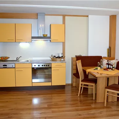A modern kitchen with yellow cabinets and hardwood flooring. The dining area is cozy, furnished with a wooden table and chairs.
