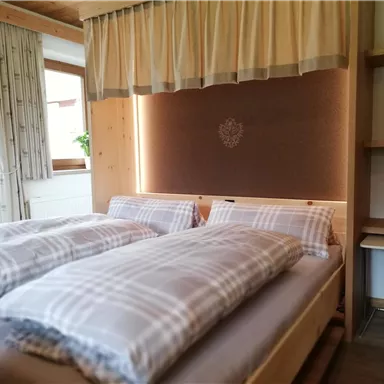 Ein gemütliches Schlafzimmer mit zwei Betten und karierten Bettdecken. Die Holzdetails und Fenster sorgen für ein warmes Ambiente.