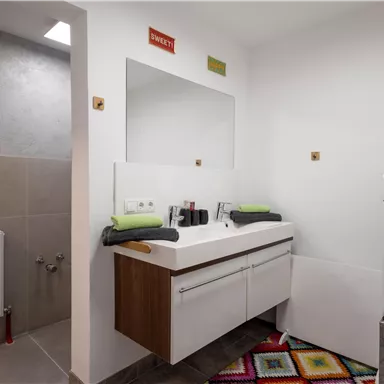 A modern bathroom with a sink and a washing machine. A colorful painting hangs on the wall and the floor is covered with a colorful carpet.
