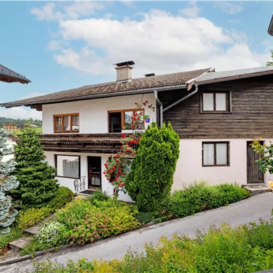 A charming house with an inviting garden.
Blooming plants all around and a clear sky give the scene a cozy atmosphere.