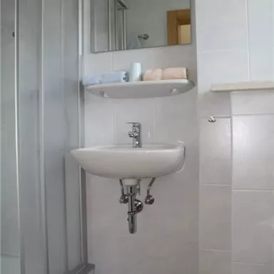 A modern bathroom with a shower and a sink. Towels are on the shelf and the floor is covered with an orange bath mat.