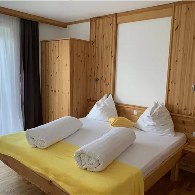 A cozy bedroom with a large bed and wooden furniture. The yellow blanket and the large windows create an inviting atmosphere.
