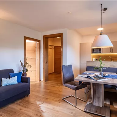 Ein modernes Wohnzimmer mit einer gemütlichen Couch und einem Esstisch. Die helle, einladende Atmosphäre wird durch das Holzdesign und die Beleuchtung unterstrichen.