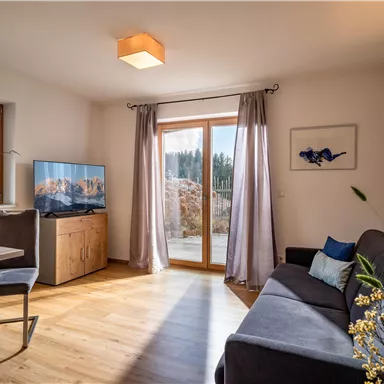 Ein modernes Wohnzimmer mit einer gemütlichen Couch und einem Tisch. Große Fenster lassen viel Licht herein und bieten einen Blick auf die Natur.