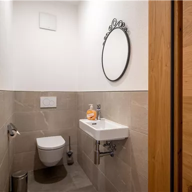 Ein modernes kleines Badezimmer mit einer hellen Wand und einer eleganten Spiegel. Die sanitären Einrichtungen sind einfach und funktional.
