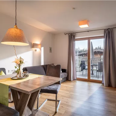 Ein modernes Wohnzimmer mit einem Esstisch und einer gemütlichen Couch. Große Fenster bieten einen Blick nach draußen auf die Terrasse.