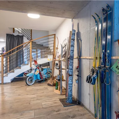 Ein modernes Foyer mit Skiern und einem alten Fahrrad. Die Wände sind in neutralen Tönen gehalten und es gibt eine Treppe im Hintergrund.