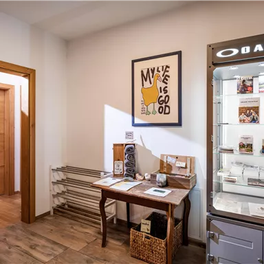 Ein einladender Raum mit Holzwänden und einem Tisch. Eine Vitrine zeigt Produkte und Zeitschriften, während ein Kunstwerk an der Wand hängt.