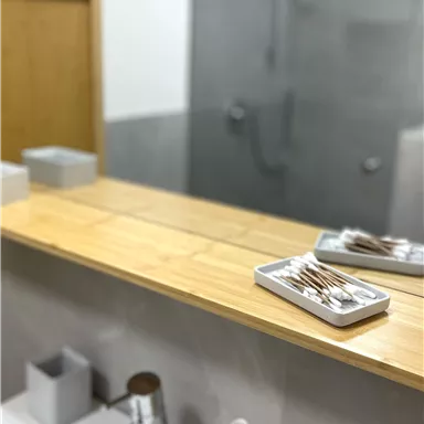 A modern bathroom with a wooden shelf and a sink. In the background, a walk-in shower can be seen.