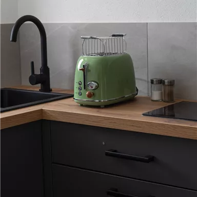 A modern toaster in a minimalist kitchen environment. The combination of a green toaster, wooden countertop, and dark cabinets creates an inviting atmosphere.