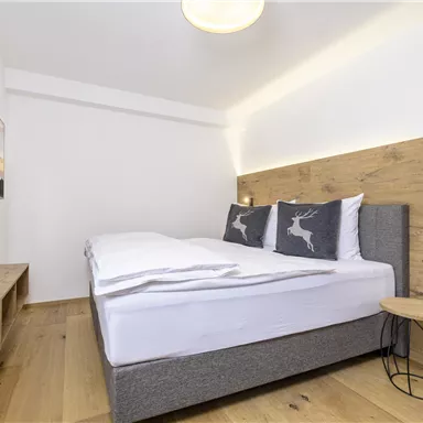 A modern bedroom with a large bed and elegant wood decoration. The walls are in neutral tones, and there is a small bedside table.