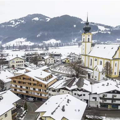 A picturesque winter landscape with snow-covered roofs and a beautiful church. The mountains in the background give the scene a charming character.