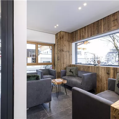 A stylish café with wooden walls and cozy seating options. Large windows offer a view of the snow-covered street.