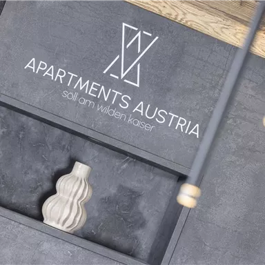 A modern reception area with the inscription "Apartments Austria". In the background, there is a decorative vase on a dark background.