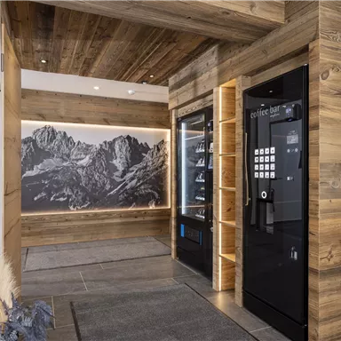 A modern interior with wooden walls and a large landscape wall. On the right side, there are two vending machines.