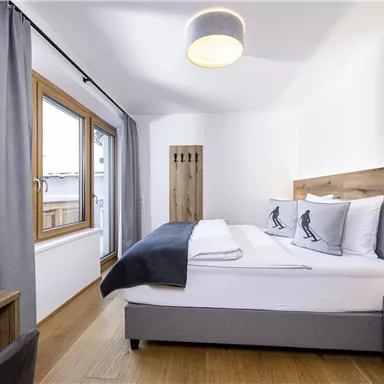 A modern bedroom with a large bed and wood details. There is a television and large windows that let in a lot of light.