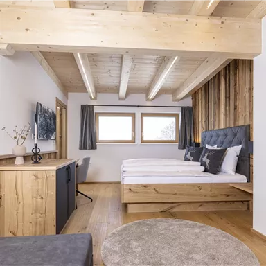 A modern bedroom with wooden paneling and a large double bed. The room is bright and friendly, with windows that provide natural light.