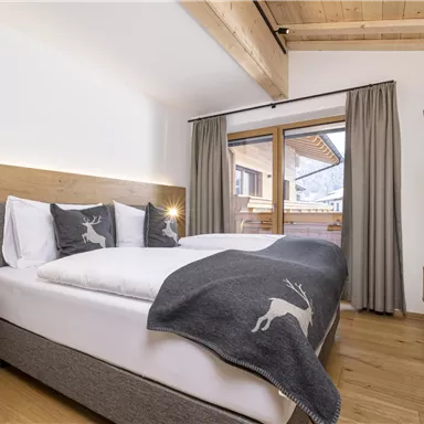 A modern bedroom with a cozy double bed and wooden elements. Large windows offer a view outside and provide plenty of daylight.