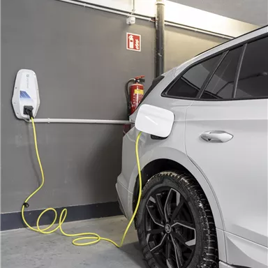 An electric car is charging at a charging station in a garage. The cable connects the vehicle to the wall box.