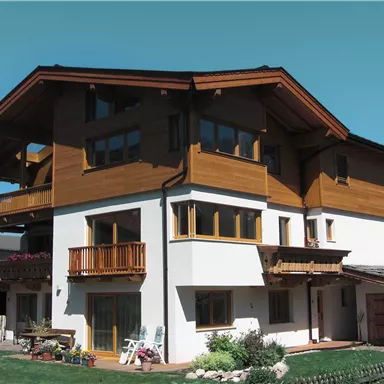 A modern house with a wood and plaster facade in the mountains. The spacious balcony and windows create a bright, inviting atmosphere.