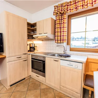Eine moderne Küche mit Holzschränken und einem großen Fenster. In der Ecke steht ein Fernseher und ein Tisch mit Stühlen.