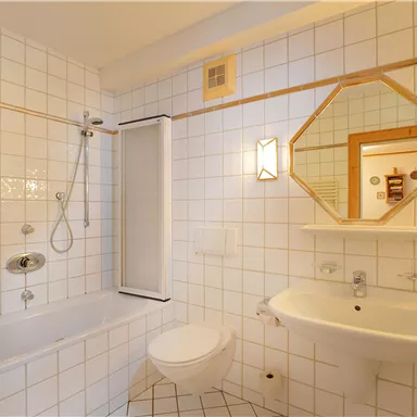 Ein helles Badezimmer mit weißen Fliesen und einem Badewannen-Duschbereich. Es gibt ein Waschbecken und einen Spiegel an der Wand.