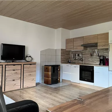 Eine moderne Küche mit Holzschränken und einem Herd. Der Raum ist hell und freundlich, mit einem Fernseher und einem Essbereich.