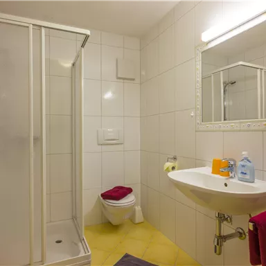 A modern bathroom with a shower, sink, and mirror. Red towels and toiletries are provided.