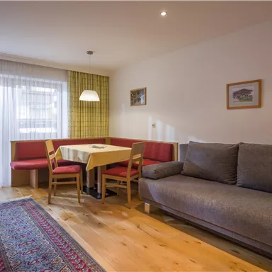 A cozy living room with a gray sofa and a dining area. Large windows let in plenty of light and provide a view outside.