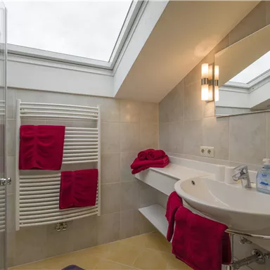 A modern bathroom with a large window and elegant fixtures. Red towels add a fresh accent to the room.