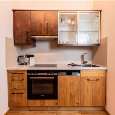 Eine moderne Küche mit Holzschränken und einer hellen Arbeitsplatte. Sie ist ausgestattet mit einem Herd, Backofen und Spüle.