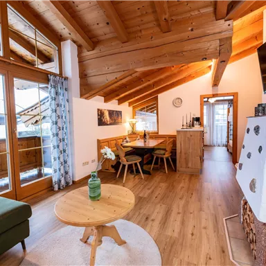 Eine moderne und gemütliche Wohnung mit Holzdecken und großen Fenstern. Der Wohnbereich ist hell und einladend, mit einem runden Tisch und einer grünen Couch.