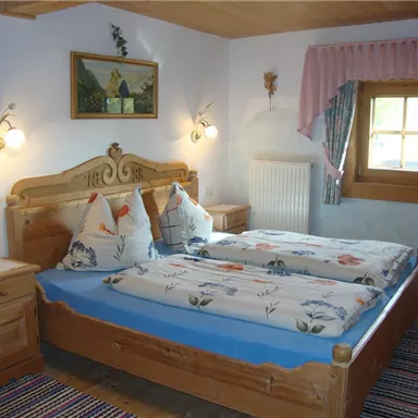 Ein gemütliches Schlafzimmer mit einem Doppelbett aus Holz und dekorativen Kissen. Die Wände sind hell und mit einem Fenster sowie einem Bild geschmückt.