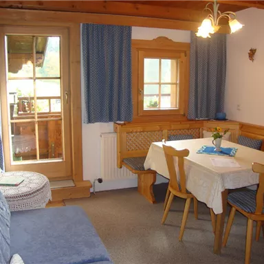 Ein gemütlicher Wohnraum mit einem blauen Sofa und einem Tisch. Die Fenster lassen viel Tageslicht herein und der Raum ist im ländlichen Stil eingerichtet.