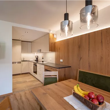 Moderne Küche mit Holzdetails und einem Esstisch. Auf dem Tisch liegen Obst und eine kleine Fernseher ist an der Wand montiert.