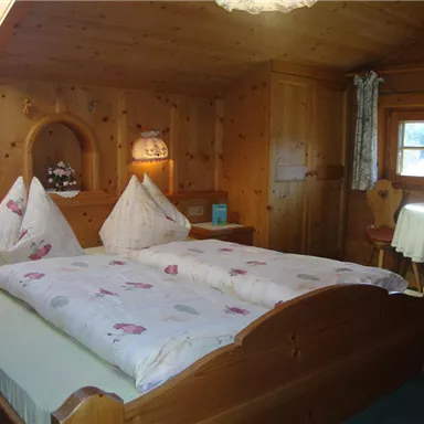 Ein gemütliches Zimmer mit einem Doppelbett und Holzverkleidung. Das Zimmer ist hell und freundlich mit dekorativen Kissen und einer kleinen Sitzecke.