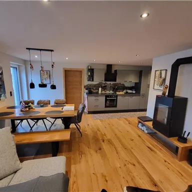 A modern kitchen with an open living area and hardwood floor. A cozy dining area with a large table and a fireplace completes the overall picture.