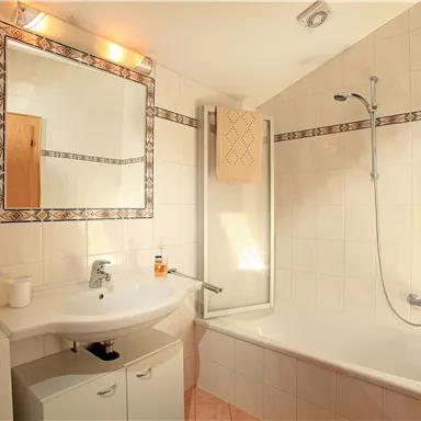 A modern bathroom with a bathtub and a shower. The room is well lit and has bright tiles.