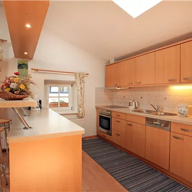 A modern kitchen with wooden cabinets and stainless steel appliances. The space is bright and inviting, with a dining area and a cozy atmosphere.