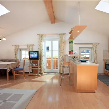 A modern, bright living kitchen with wooden floors and high ceilings. There is a dining area, a fully equipped kitchen, and large windows for plenty of daylight.