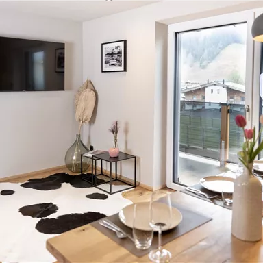 A modern living room with a television and a large window. The room is decorated with a cowhide and a dining table, creating a cozy atmosphere.