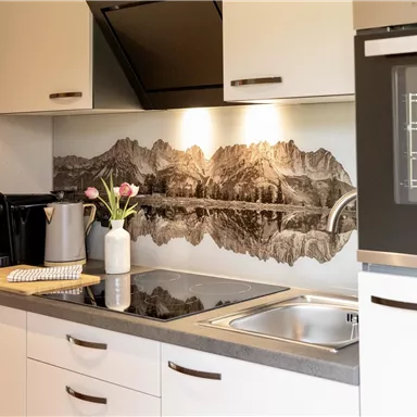 A modern kitchen with white cabinets and an elegant black stove. In the background, there is an impressive mountain motif on the wall.