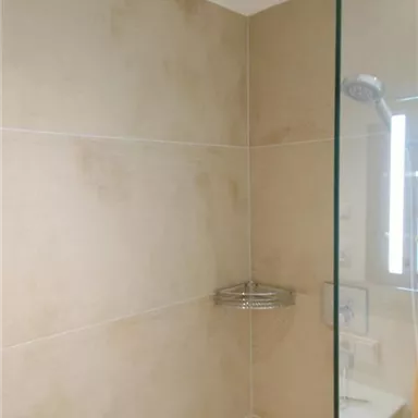 A modern shower with beige tiles and a glass wall. The rain shower head is mounted on the ceiling.