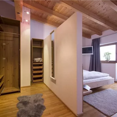 A modern room with a wooden ceiling and a cozy bed. There is a wardrobe and access to a balcony with a view.