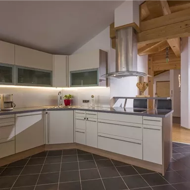 A modern kitchen with light cabinets and black countertops. It features a central cooking island and has a cozy atmosphere.